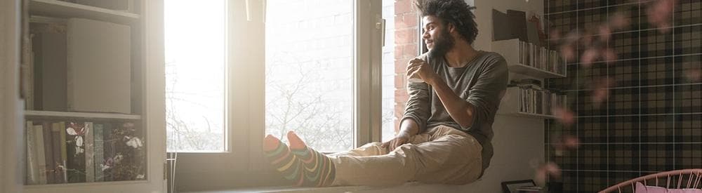 Hombre sentado con sus piernas en el alféizar de una ventana bebiendo café