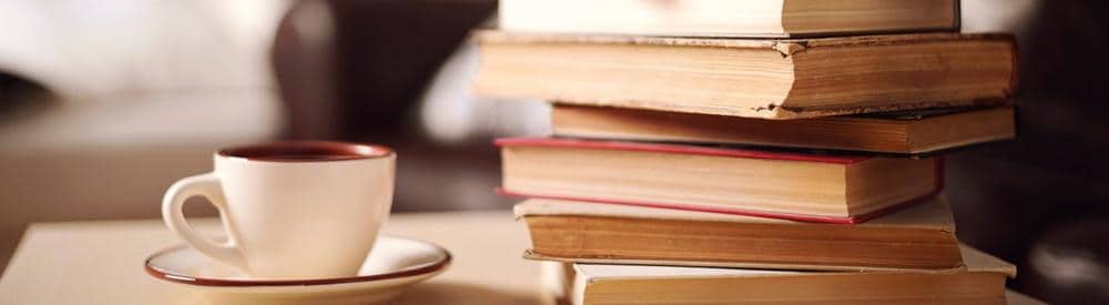 Una pila de libros junto a una taza de café en un platillo